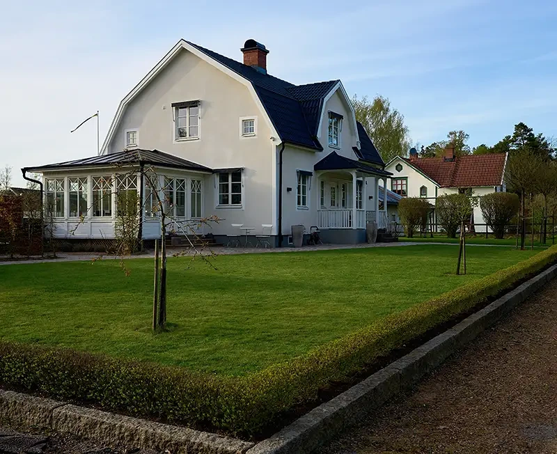 Vitt tvåplanshus med svart tak och inglasad veranda vid grön gräsmatta.